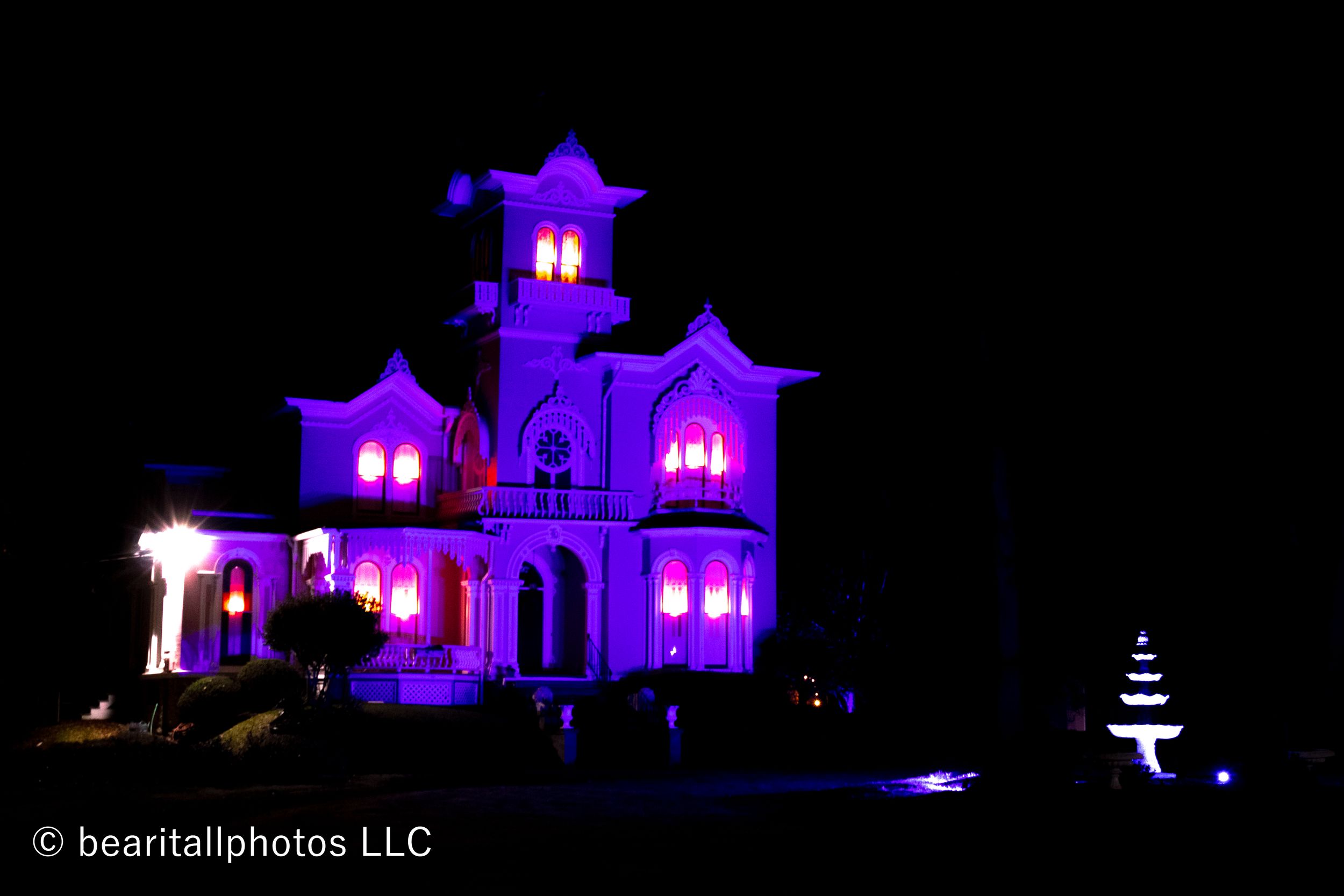Victorian mansion illuminated in purple lighting at night.