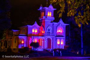 Historic house lit dramatically with blue and pink lights creating an eerie nighttime atmosphere.