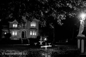 Nighttime view of historic mansion with illuminated windows and classical statuary.