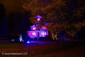 Autumn trees frame a distant Victorian house lit in purple and pink hues.