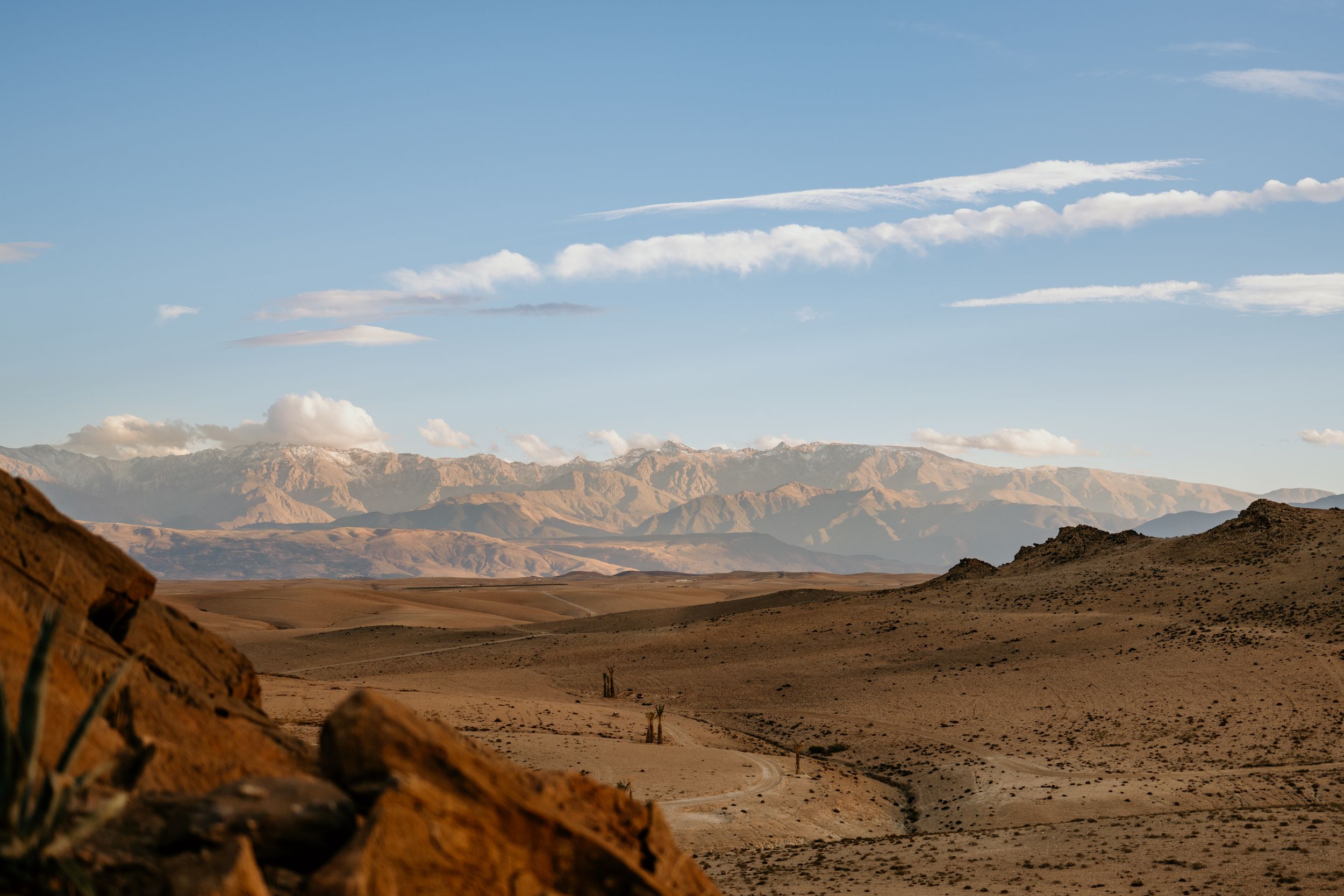 Vast desert terrain with rocky outcrops under a bright blue sky with scattered clouds.