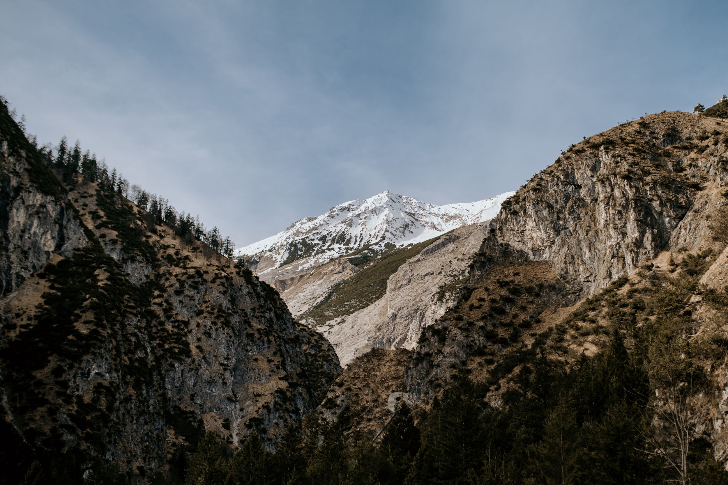 Snow-capped mountain peaks rise against a clear blue sky in a rugged wilderness landscape.