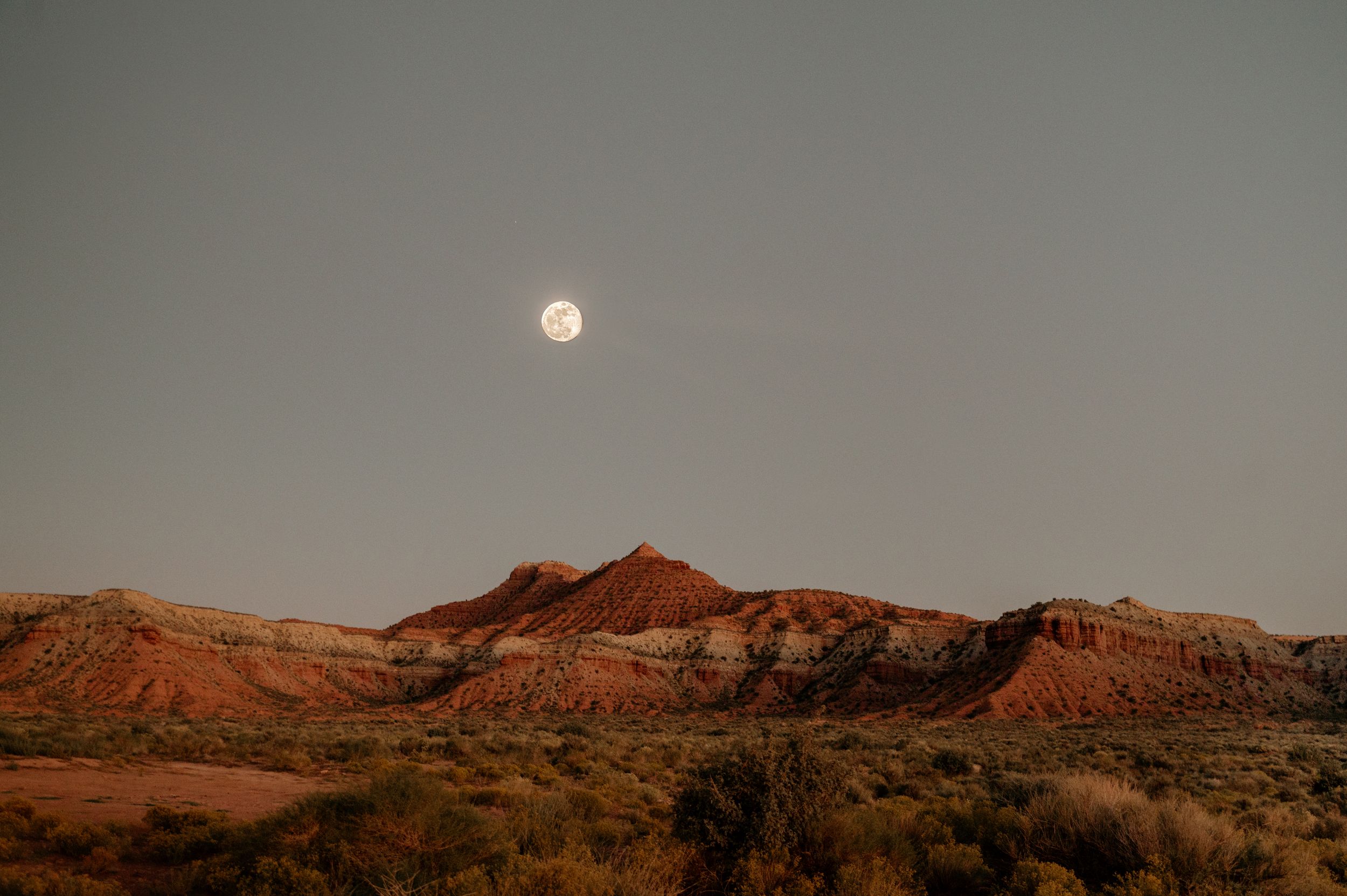 Desert landscape at sunset with red rock formations and a full moon rising in the distance.