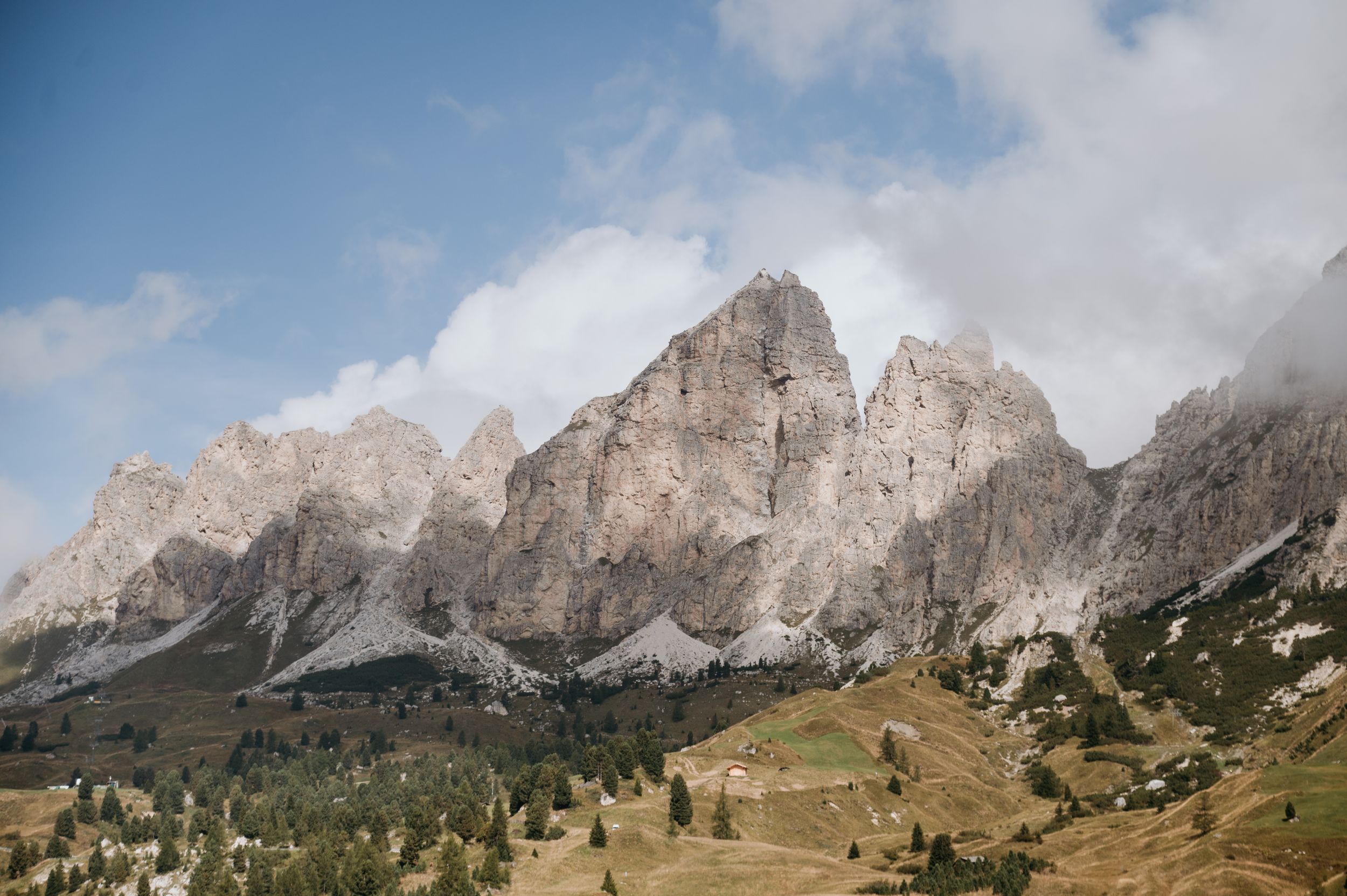Jagged Dolomite mountain peaks rise above green meadows under partly cloudy skies.