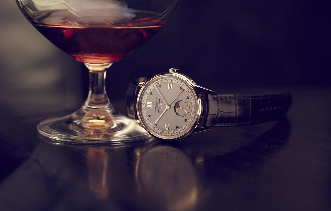 Wine glasses and timepiece arranged on dark surface with dramatic lighting.