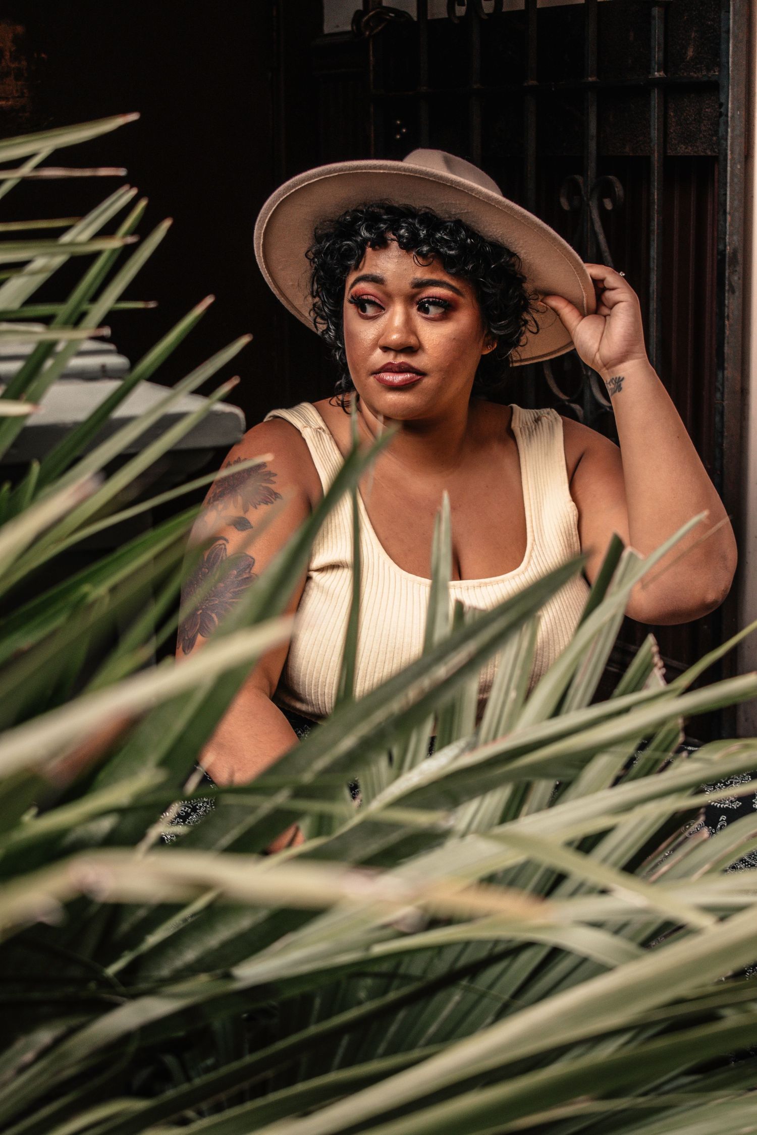 Person in sun hat and striped top poses behind tropical palm fronds.