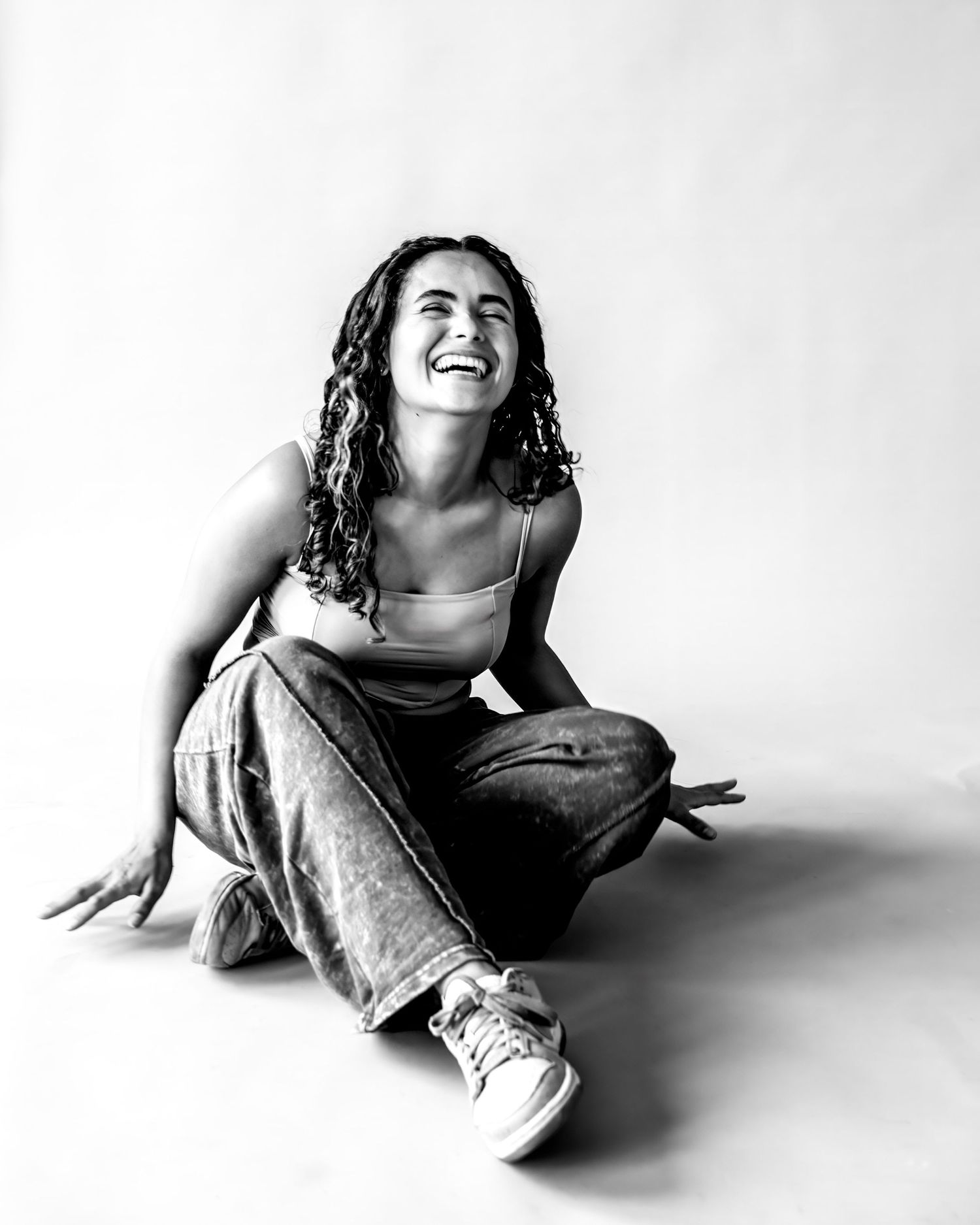 Black and white portrait series showing a person in casual clothing lying down and laughing against a white background.