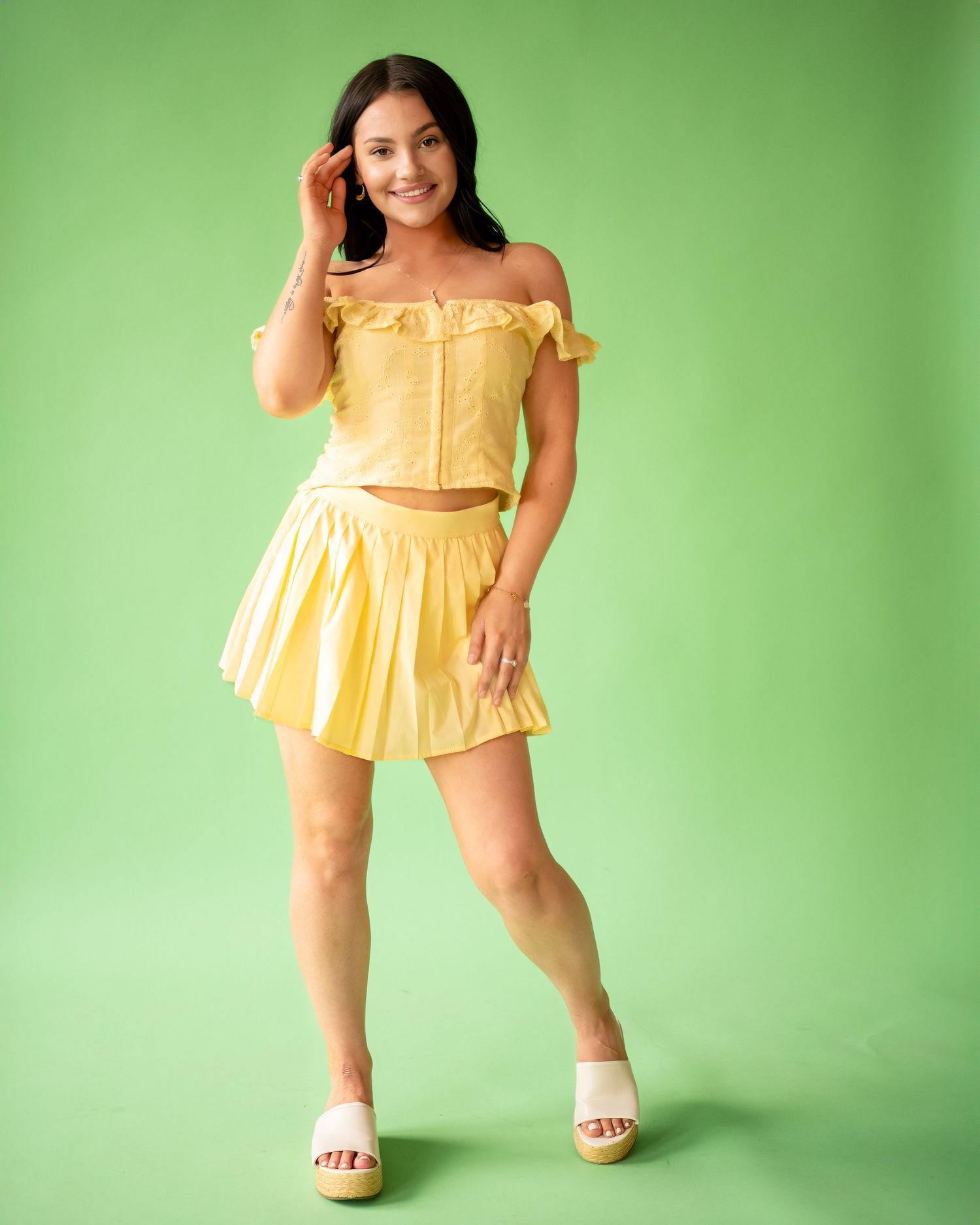 A young girl in a yellow ruffled dress poses playfully against a green studio backdrop.