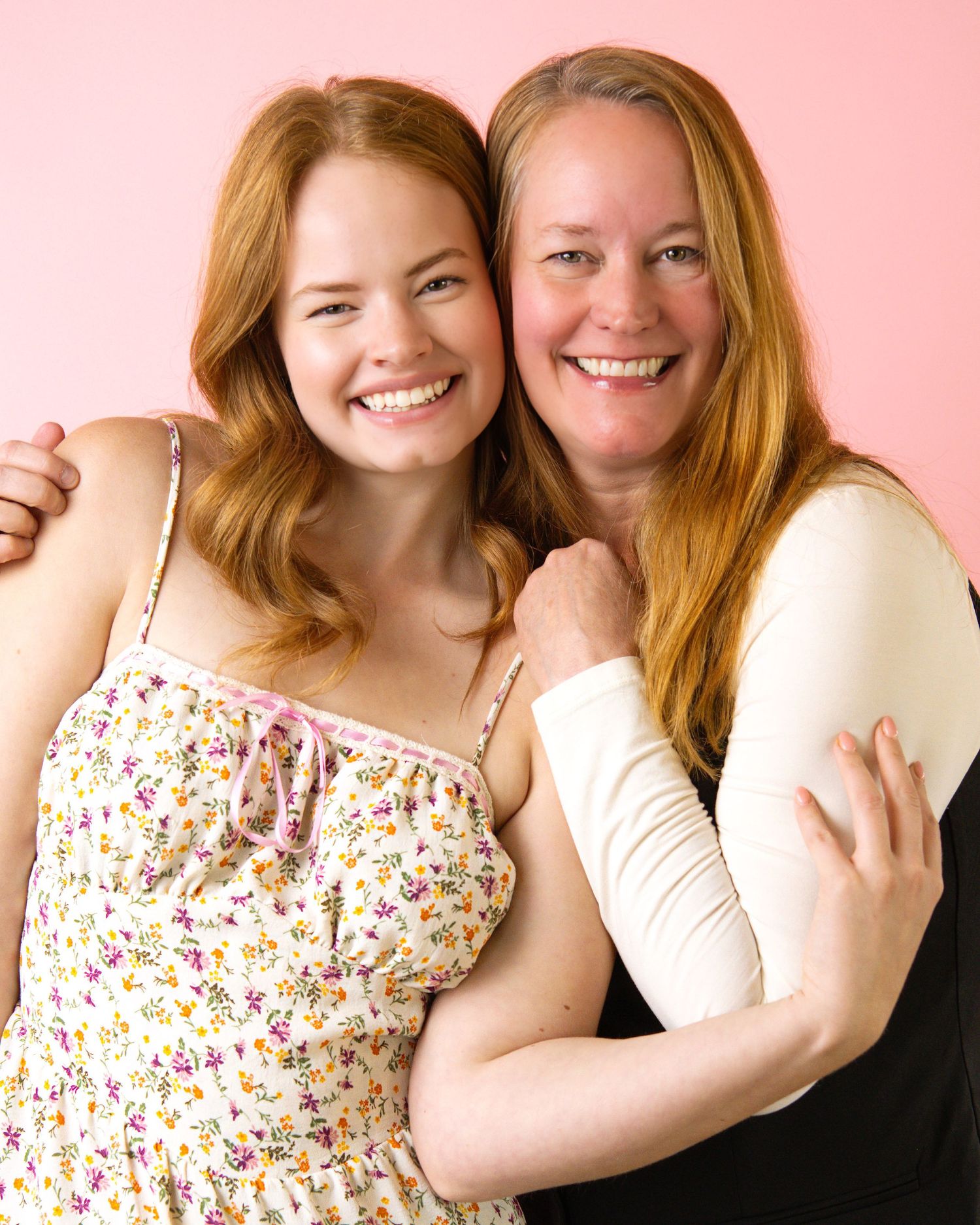 Two people in matching outfits smile and embrace against a pink background in a series of candid portrait poses.
