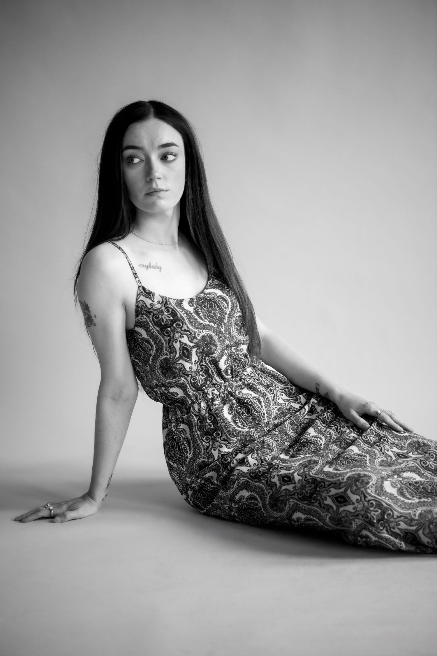 Black and white portrait of a person in a patterned dress lying on the floor in an artistic pose.