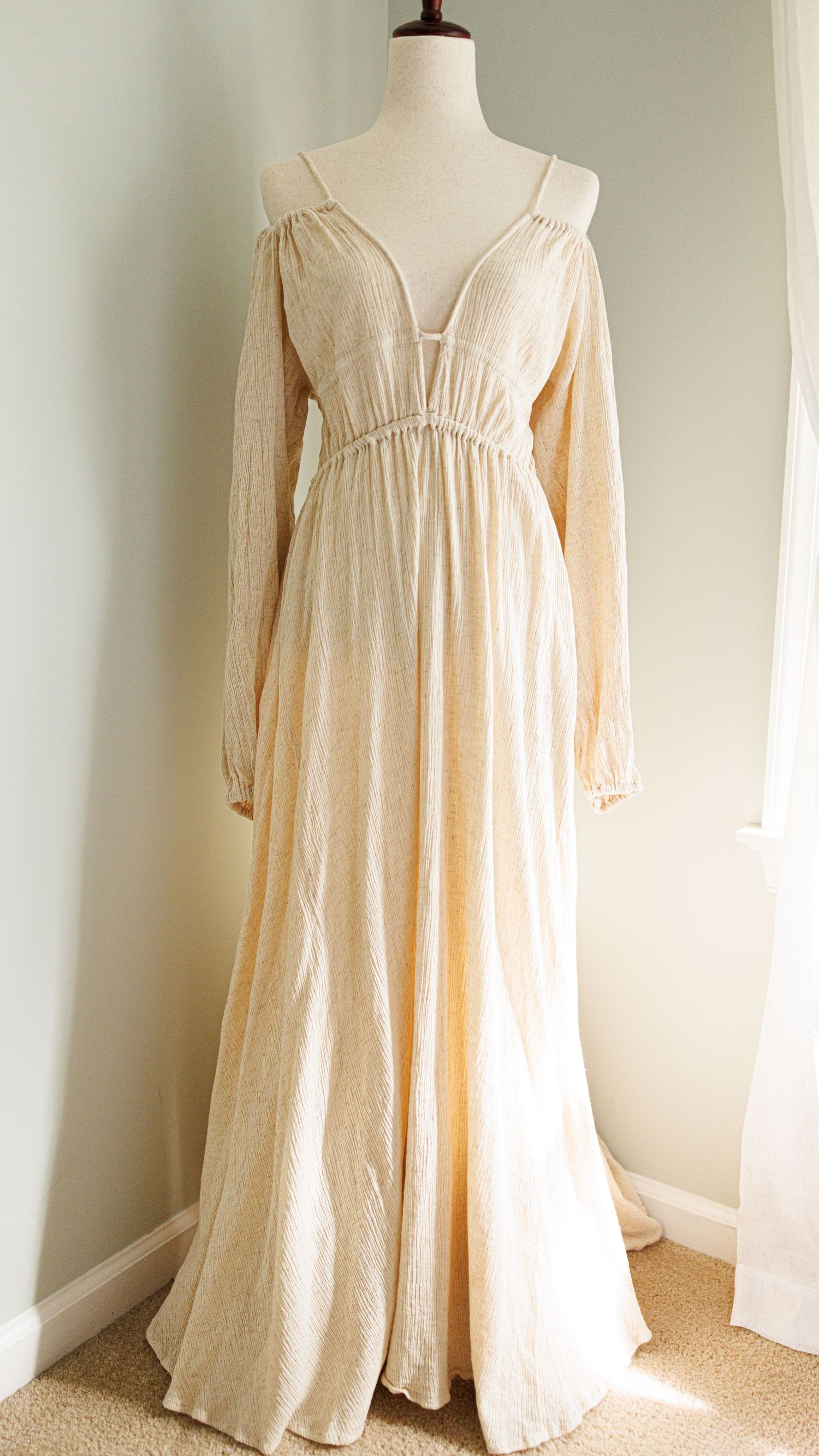 Vintage cream-colored maxi dress with puff sleeves and gathered neckline displayed on white mannequin against pale wall.