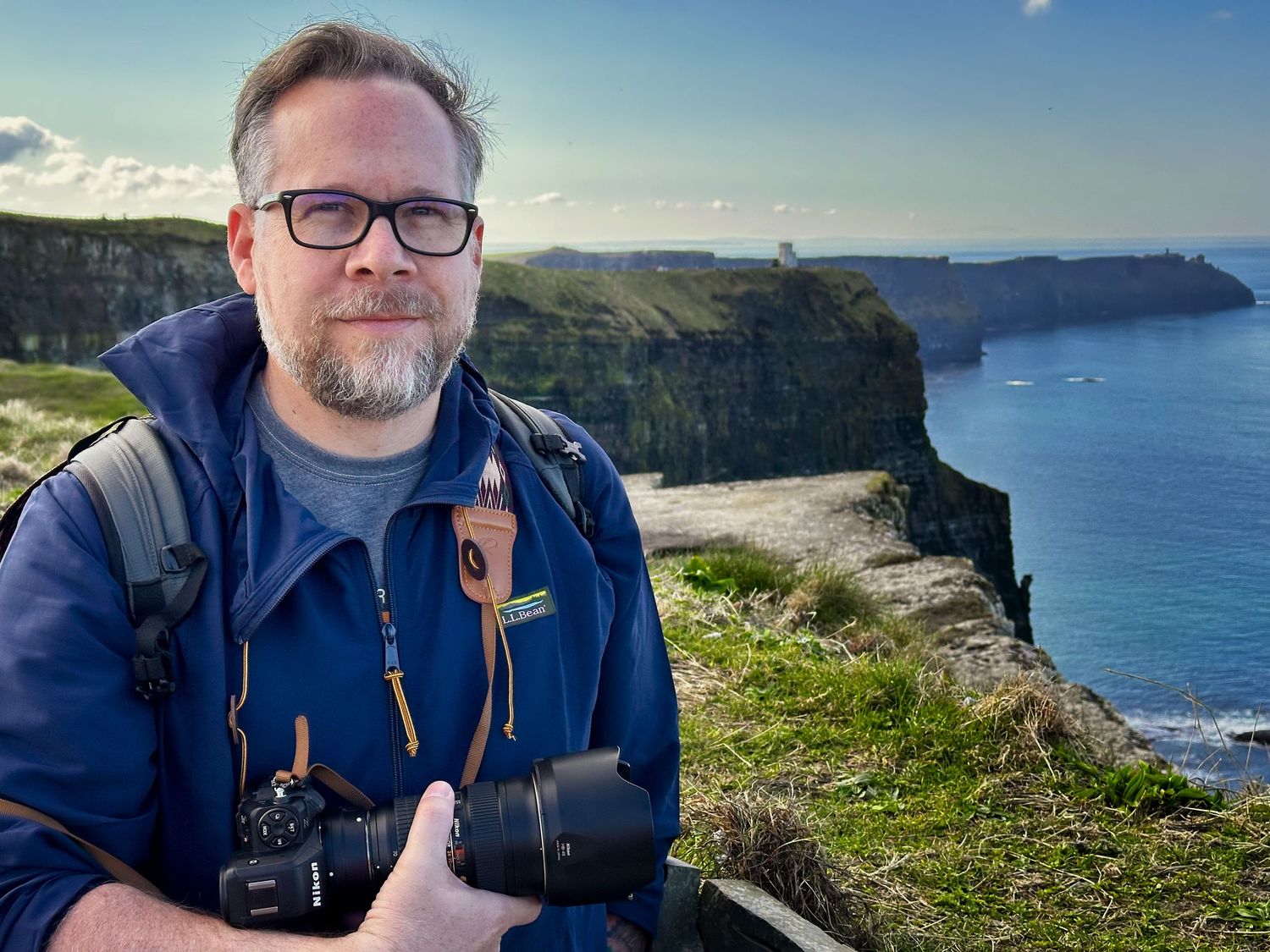 Photographer Ashley Bell with camera gear overlooking dramatic coastal cliffs and ocean views at the Cliffs of Moher.