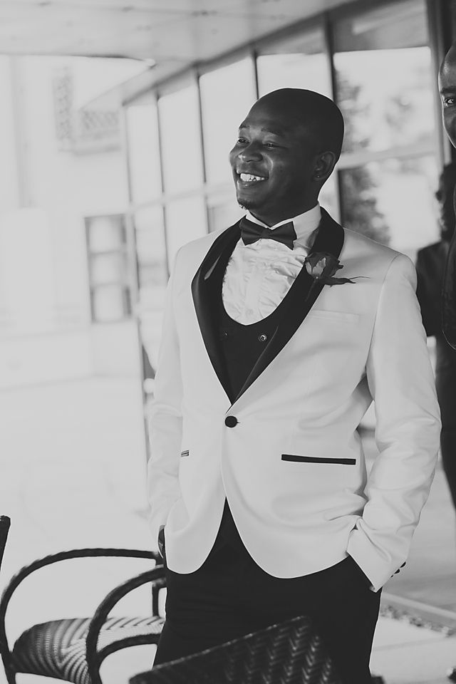 Groomsmen in white tuxedo jackets and black bowties share laughs during wedding celebration.