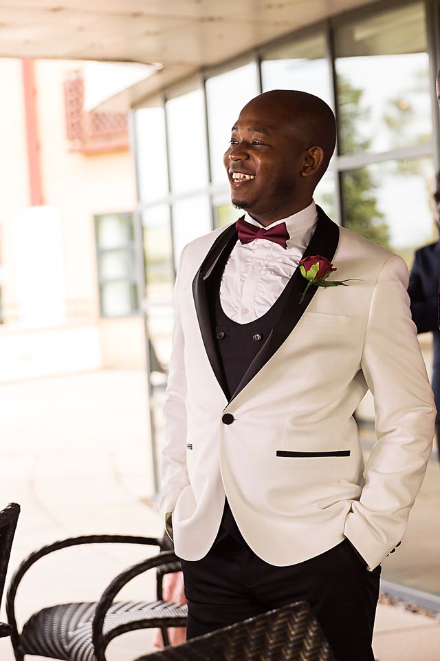 Groom in elegant white tuxedo jacket with black lapels smiles during wedding celebration.