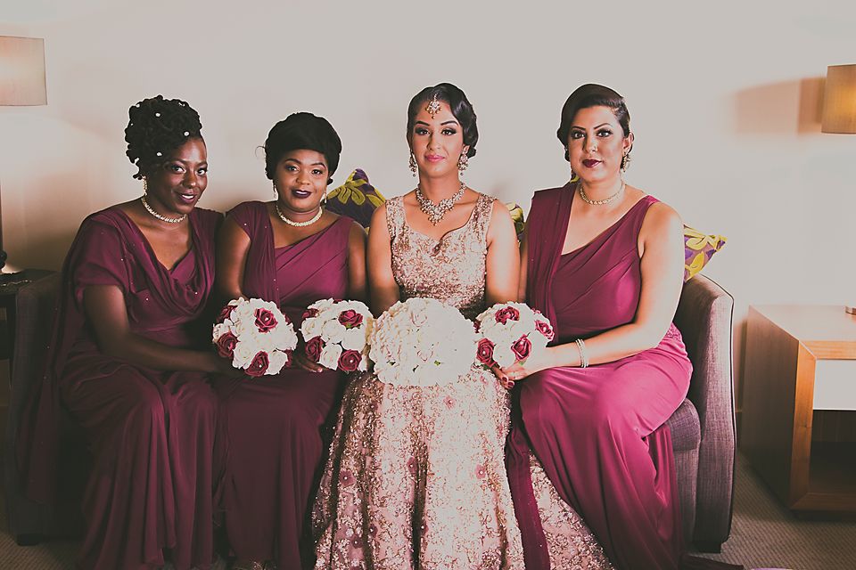 Bridesmaids in burgundy dresses pose with bride in floral gown holding bouquets.