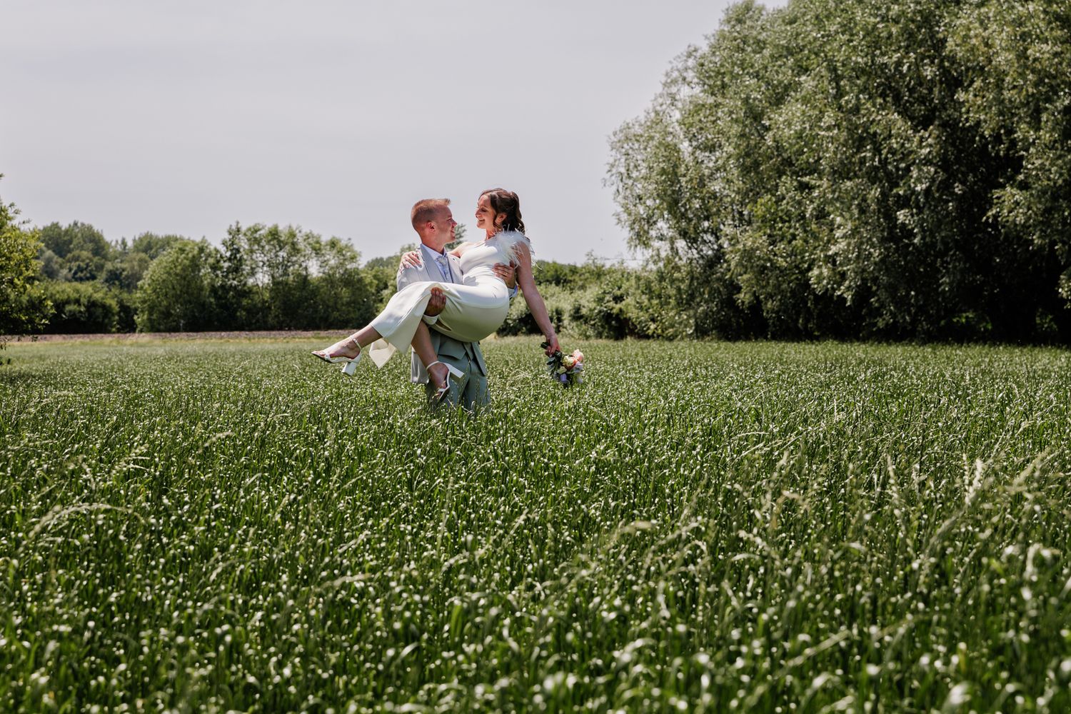 Bruidegom draagt de bruid door een groen veld.