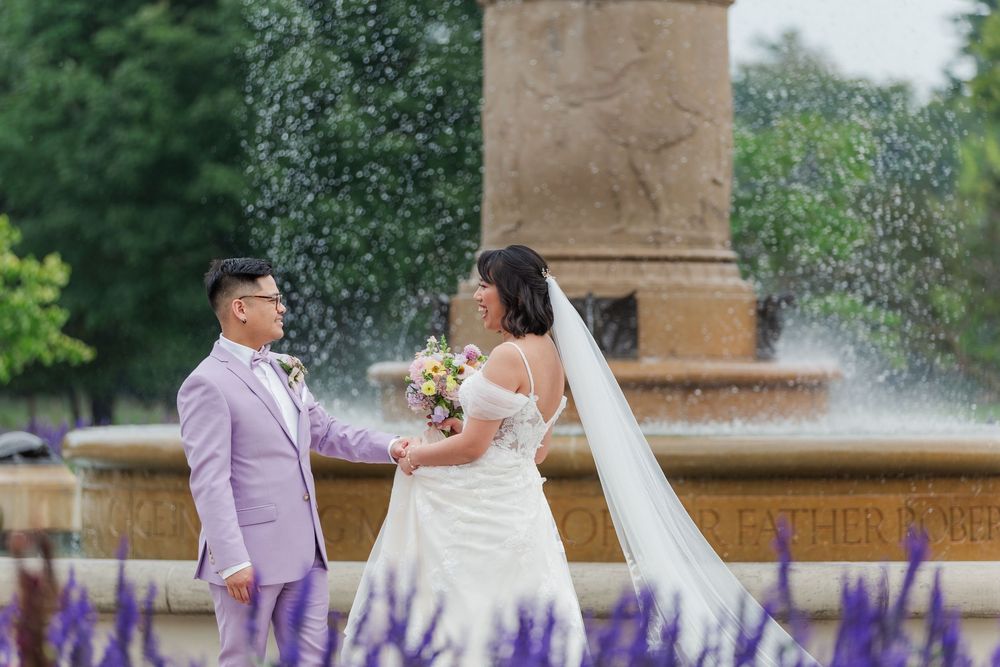 Bride and groom dance in front of a grand fountain surrounded by purple flowers at Gage Park in Hamilton, Ontario.