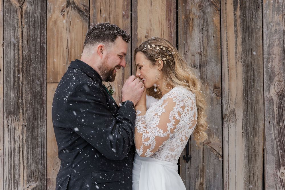 Bride and groom snuggle close to stay warm in front of a wooden wall outside during a winter wedding at Cellar 52 in St. Jacobs, Ontario.
