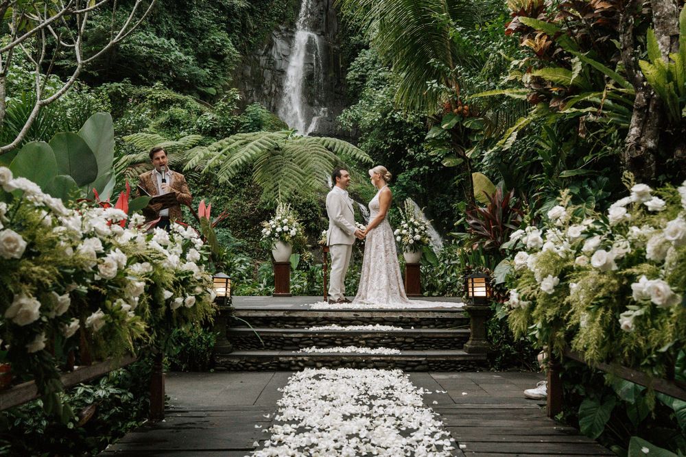 Lush garden wedding ceremony setup with white floral arrangements and stone steps surrounded by tropical greenery.
