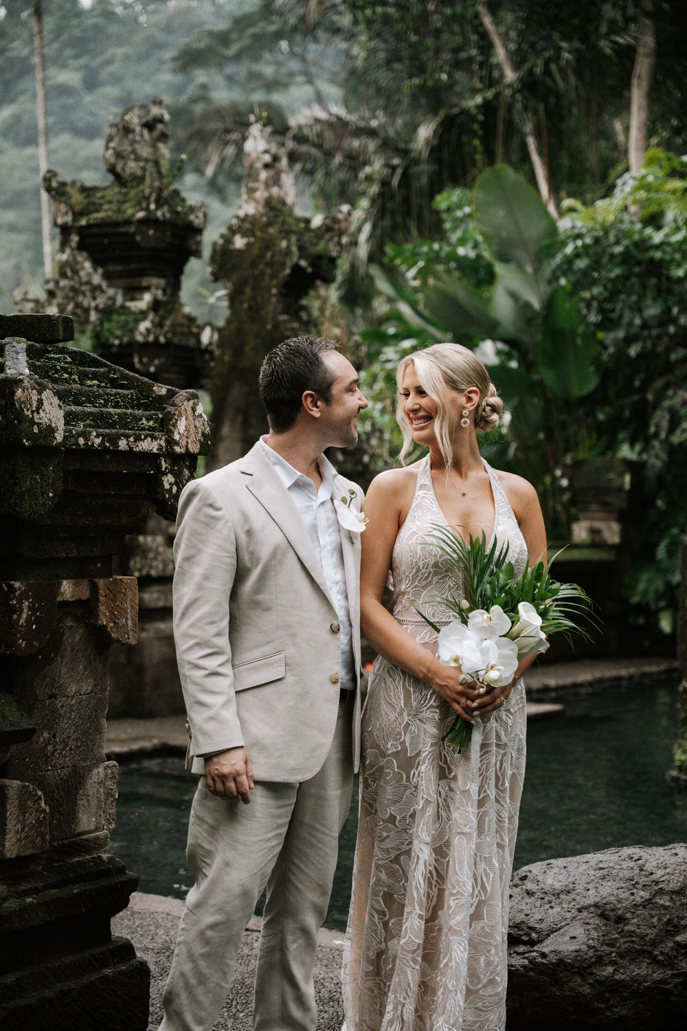A couple in light colored wedding attire share joyful moments together in a lush tropical garden setting.