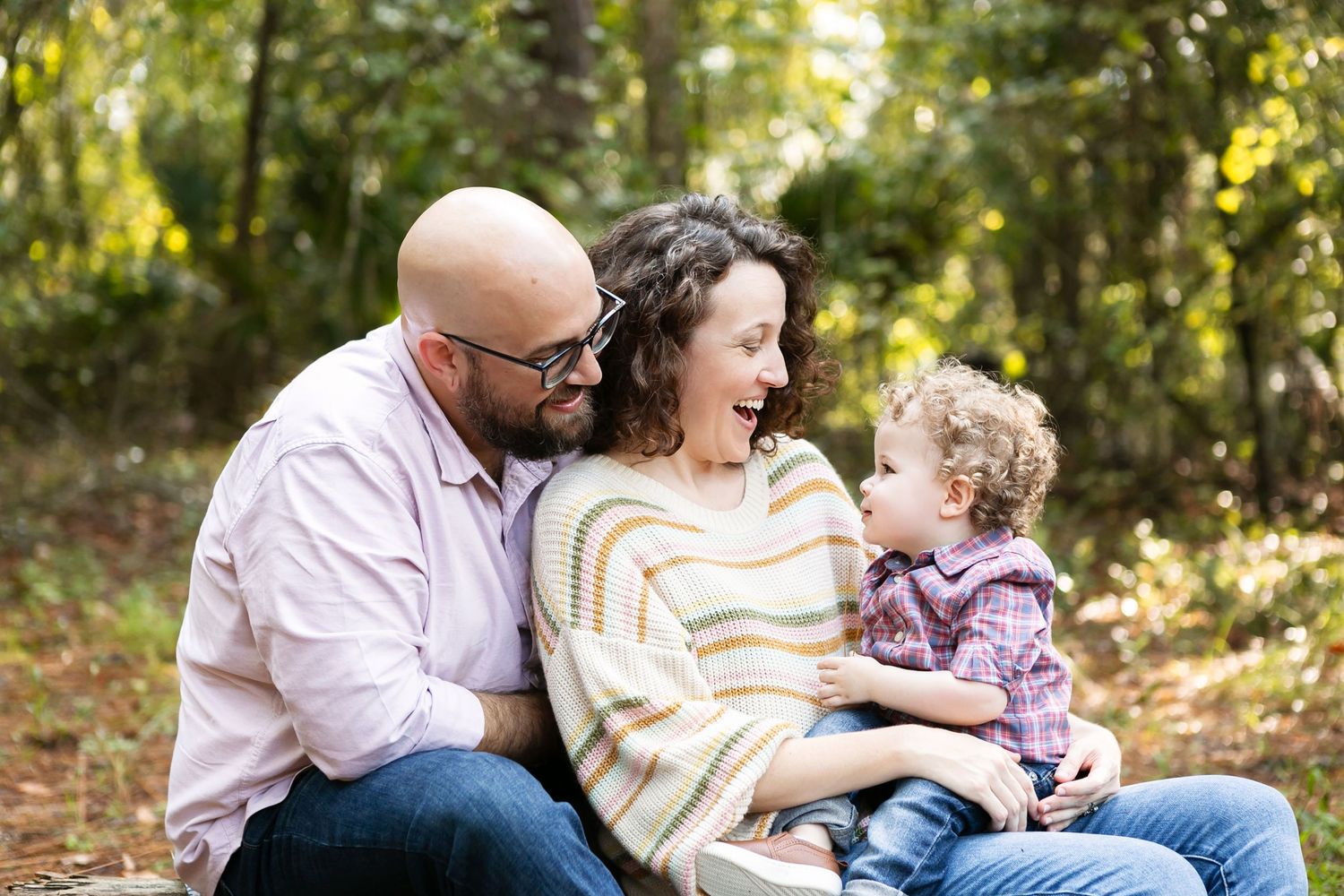 Family sitting together on tree trunk in sunlit forest during outdoor photo session. Orlando Family Photography, Sanford Family Photography