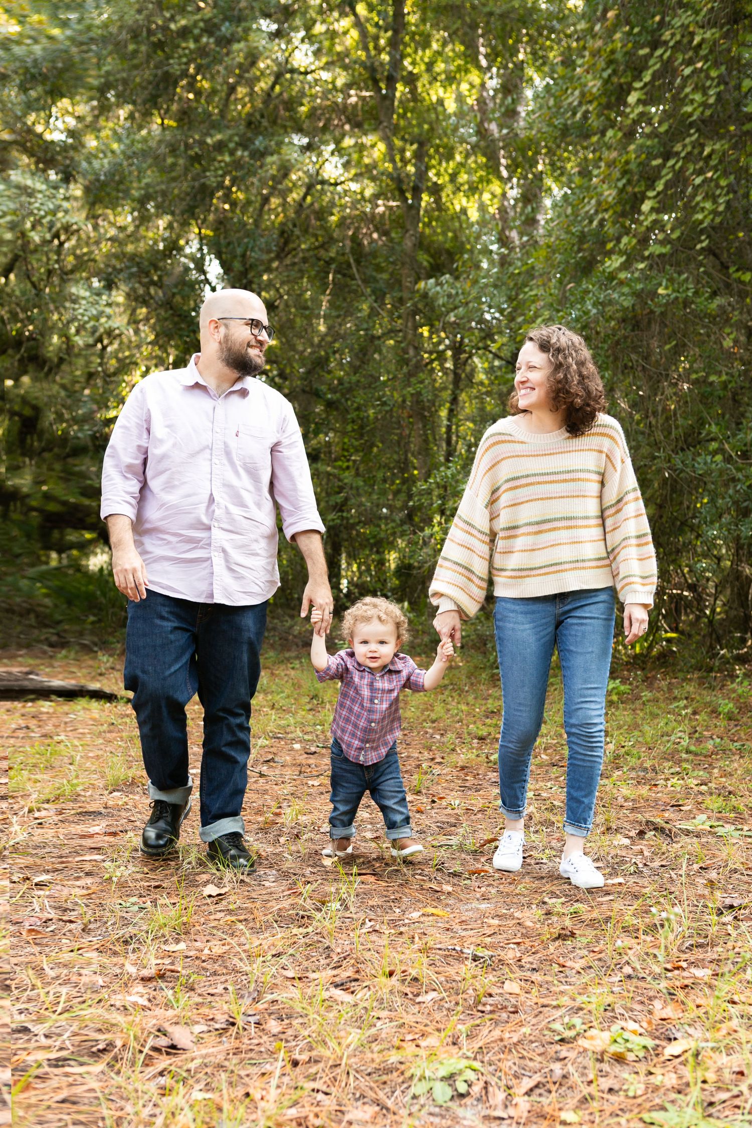 A family walks together holding hands on a wooded path on an autumn day. Orlando Family Photography, Sanford Family Photography