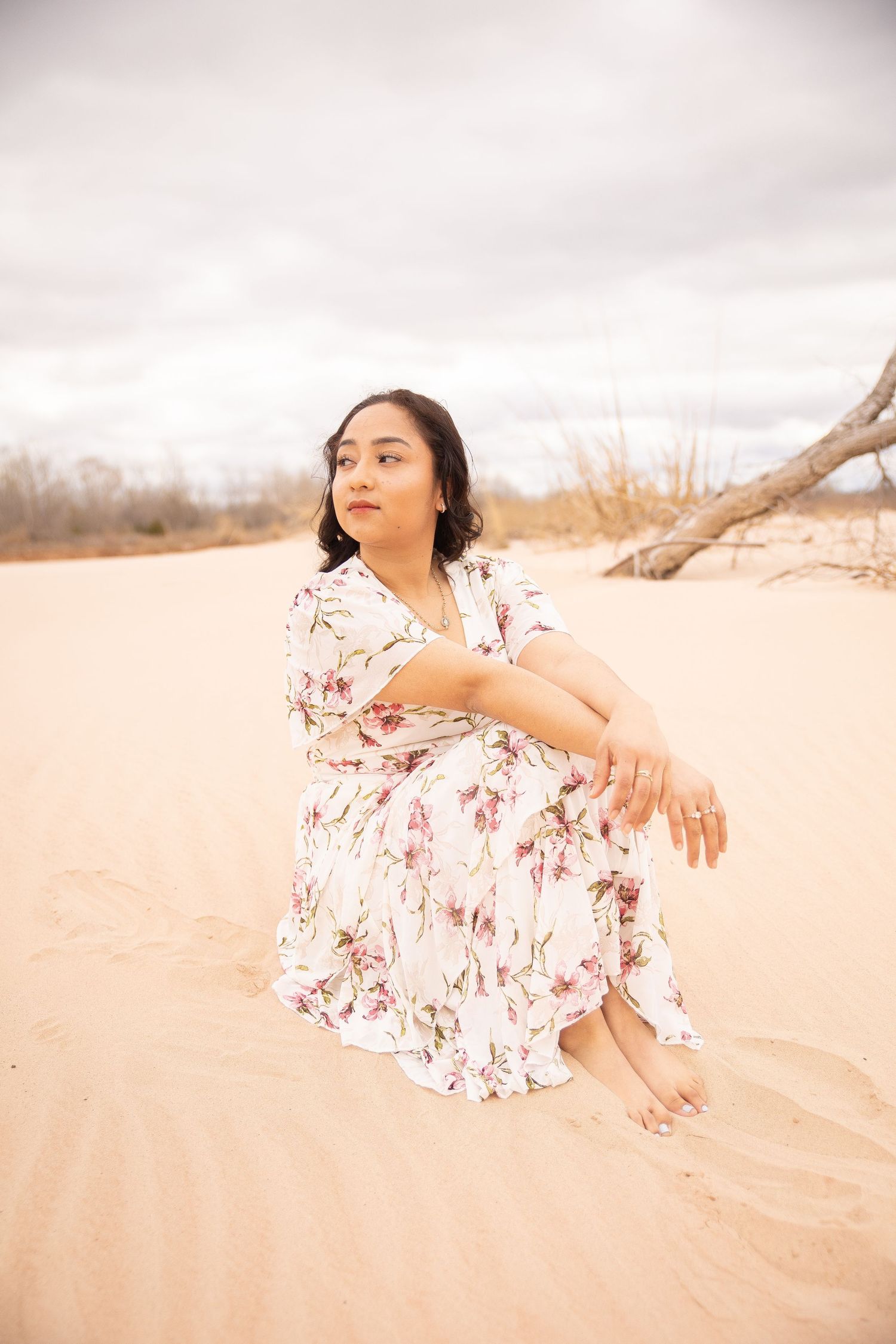 A person in a flowy white and red floral dress poses gracefully in a desert landscape during sunset.