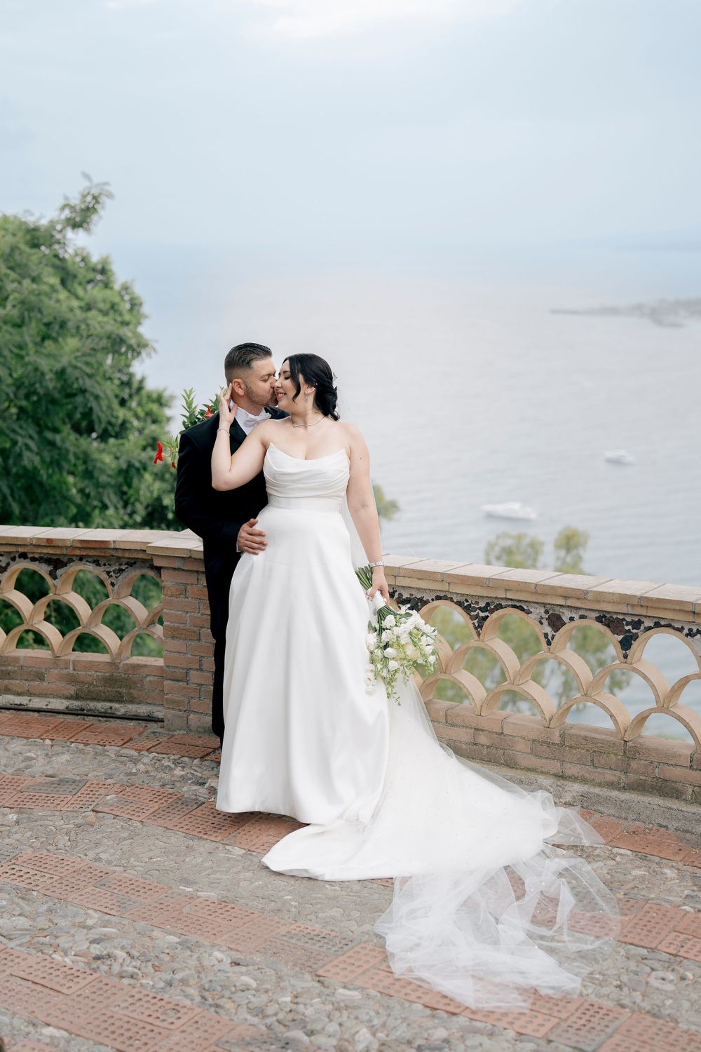 A romantic wedding portrait on a brick terrace overlooking a scenic waterfront view.