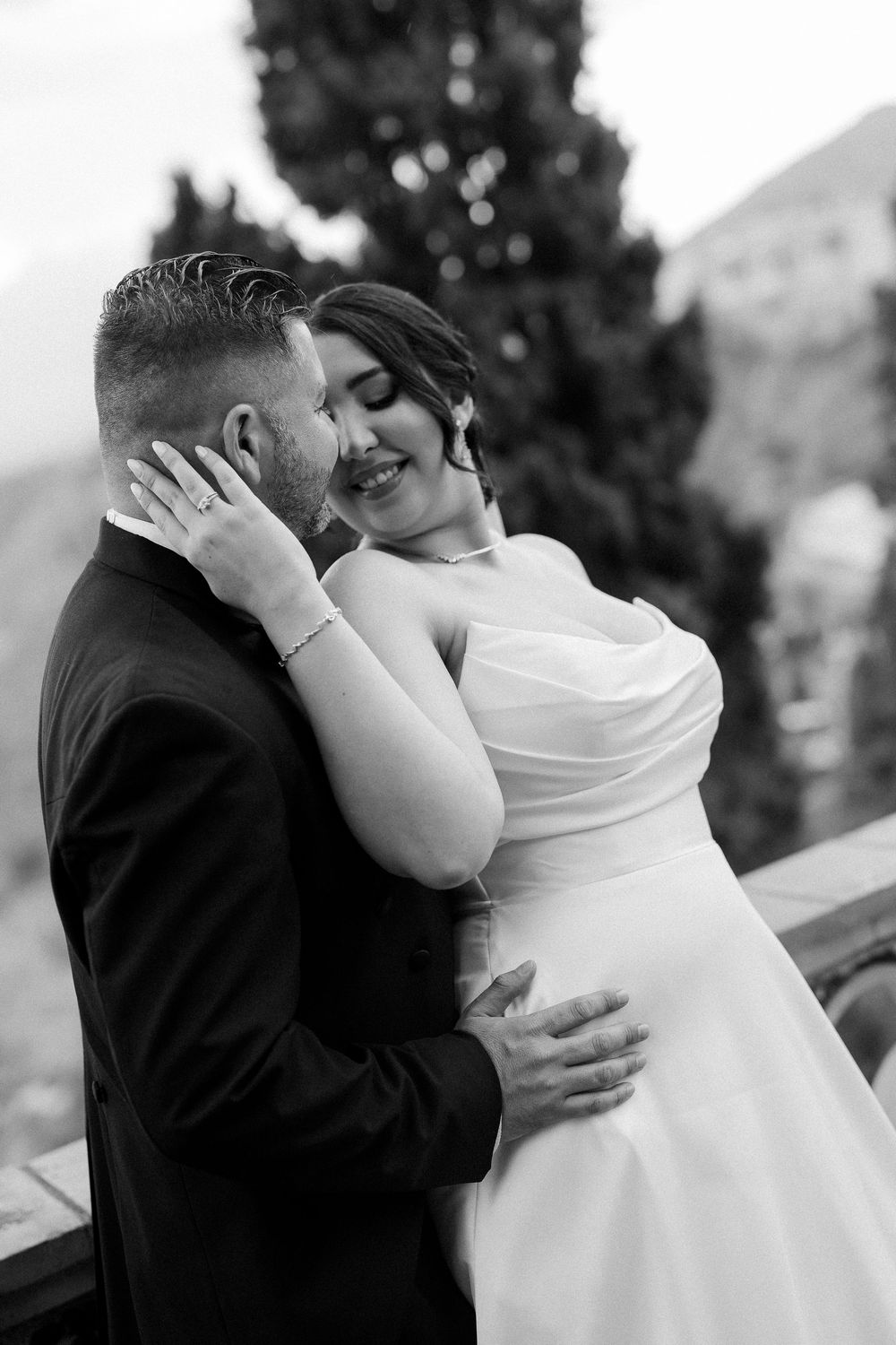 A tender black and white wedding moment captured showing a romantic embrace on a balcony with mountains in background.
