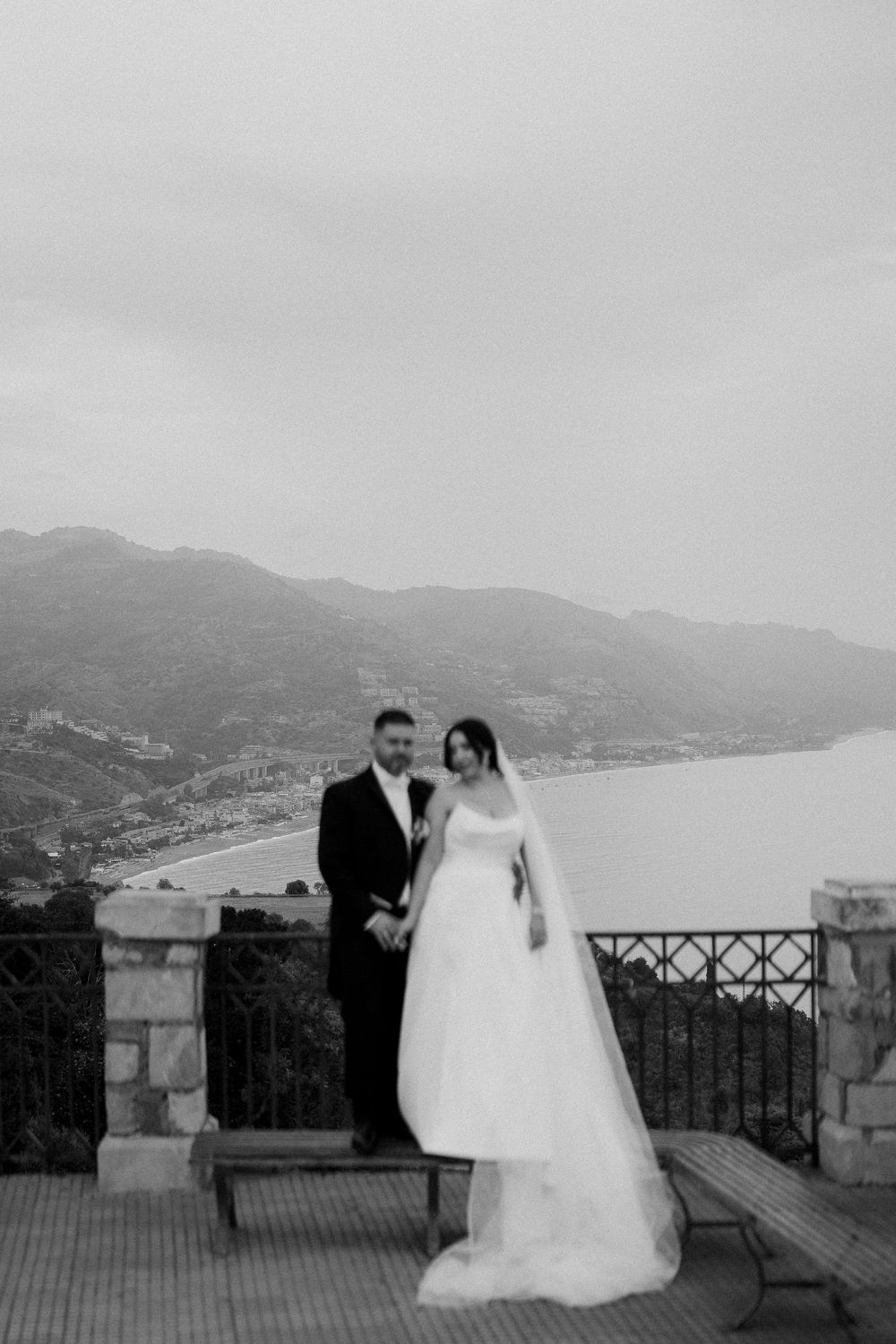 A black and white wedding photoshoot sequence showing a couple posing on a scenic mountain overlook with coastal views.