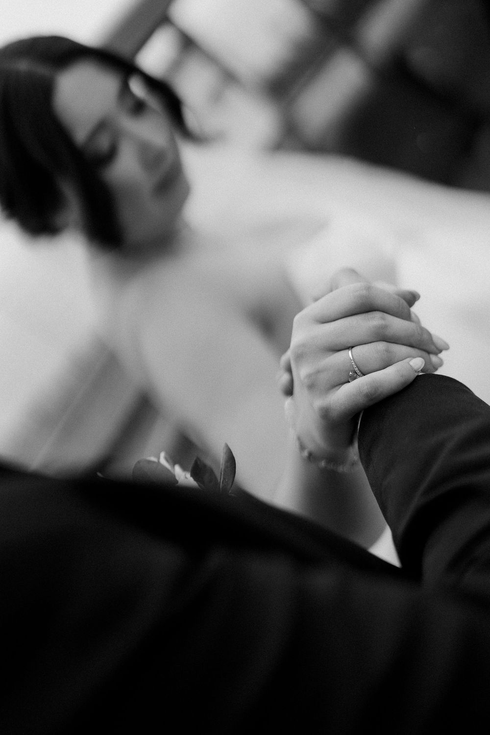 Black and white close-up of clasped hands showing wedding rings.
