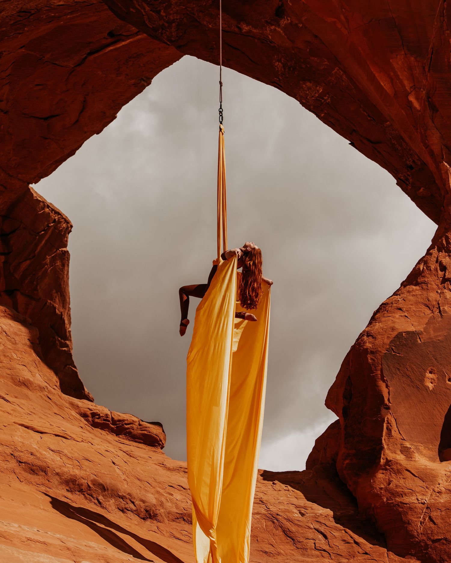 Aerialist mid-pose on silks in a Utah red rock arch; modern aerial arts imagery blending natural beauty with strong aerial shapes