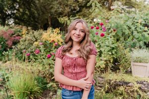 Someone in a red ruffled top and jeans poses in a lush garden setting with blooming flowers and greenery.