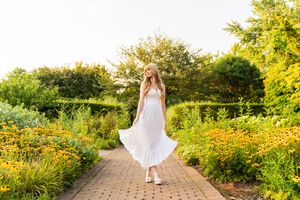 A garden path winds through vibrant yellow wildflowers and lush greenery on a sunny summer day.