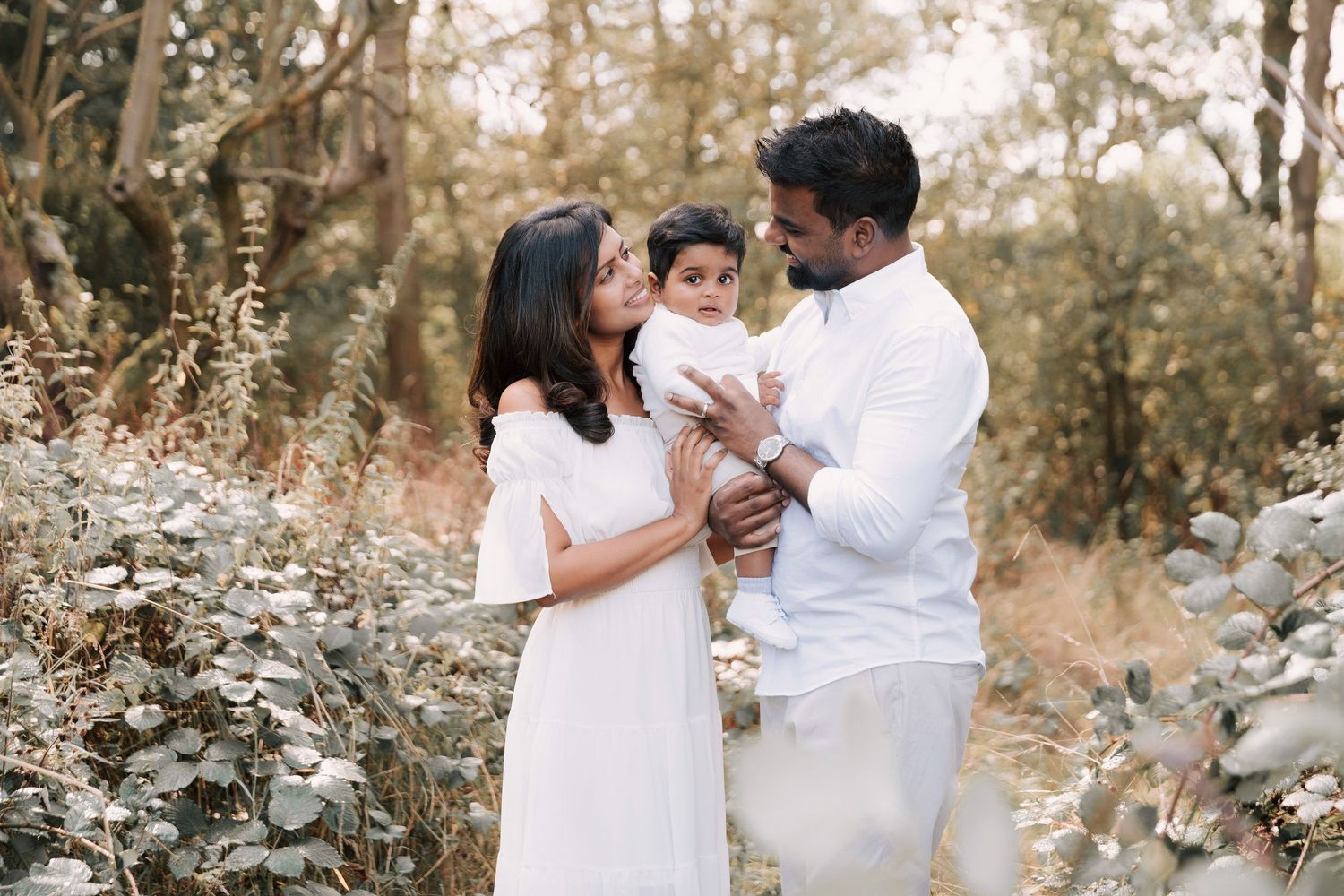 Family wearing white outfits poses together in outdoor nature setting with soft golden light.