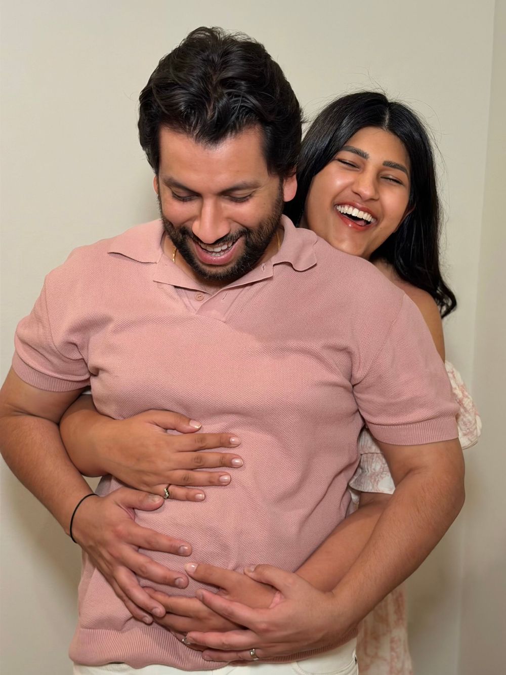 Two people in pink and white clothing share playful hugs and laughter indoors.