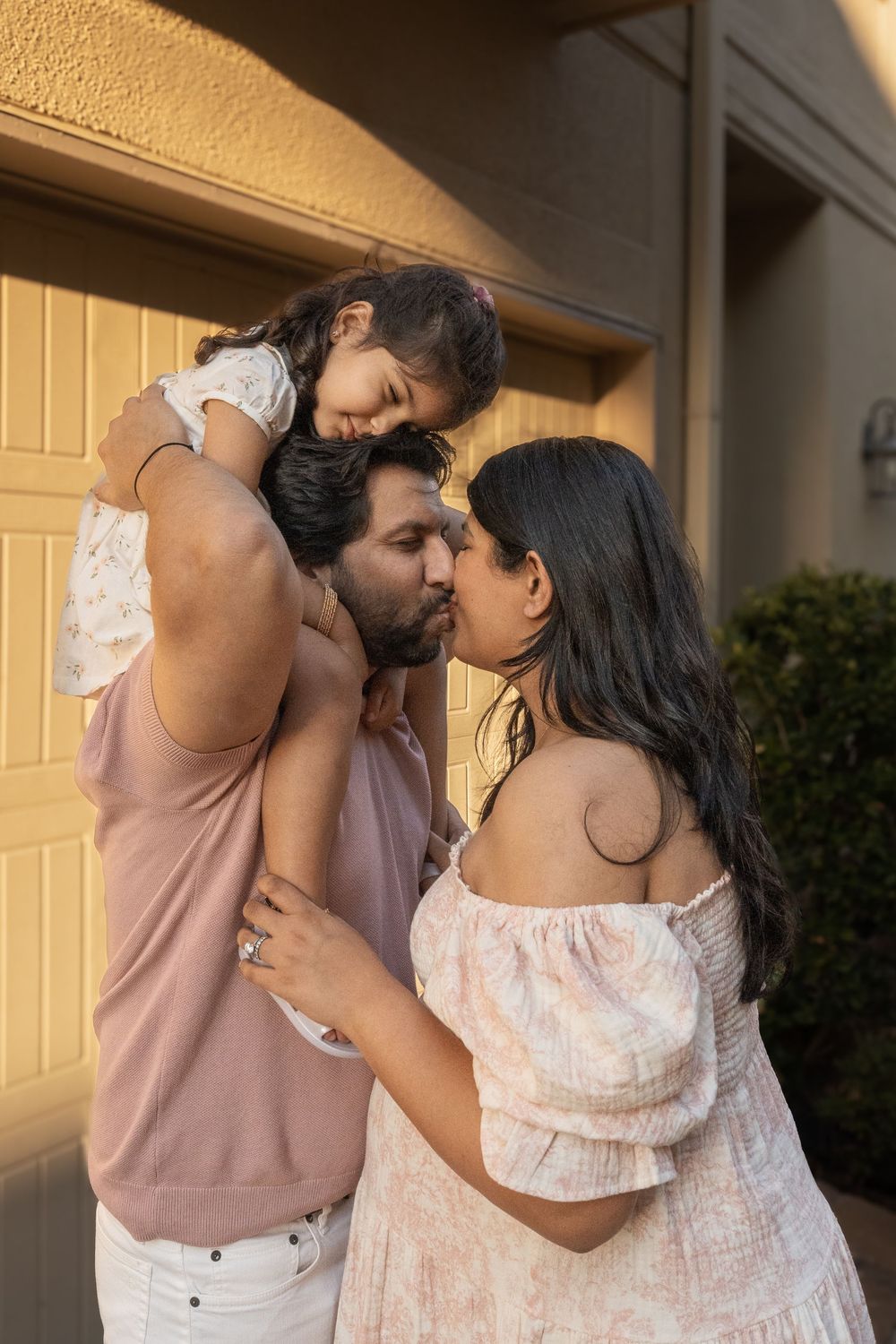 Family sharing an intimate moment outdoors at sunset with child on shoulders.
