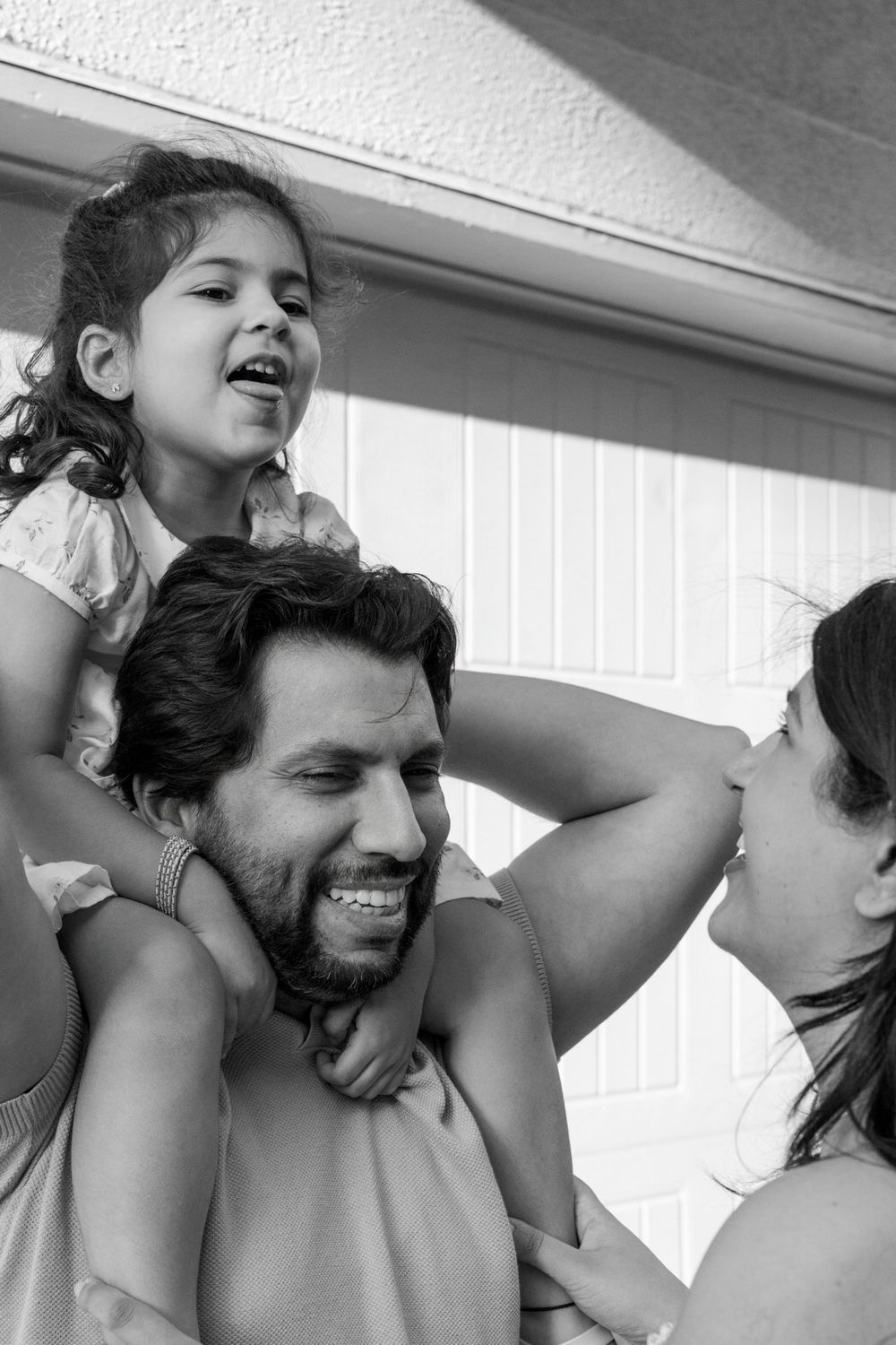 Black and white candid family moment with child riding on shoulders during playtime.