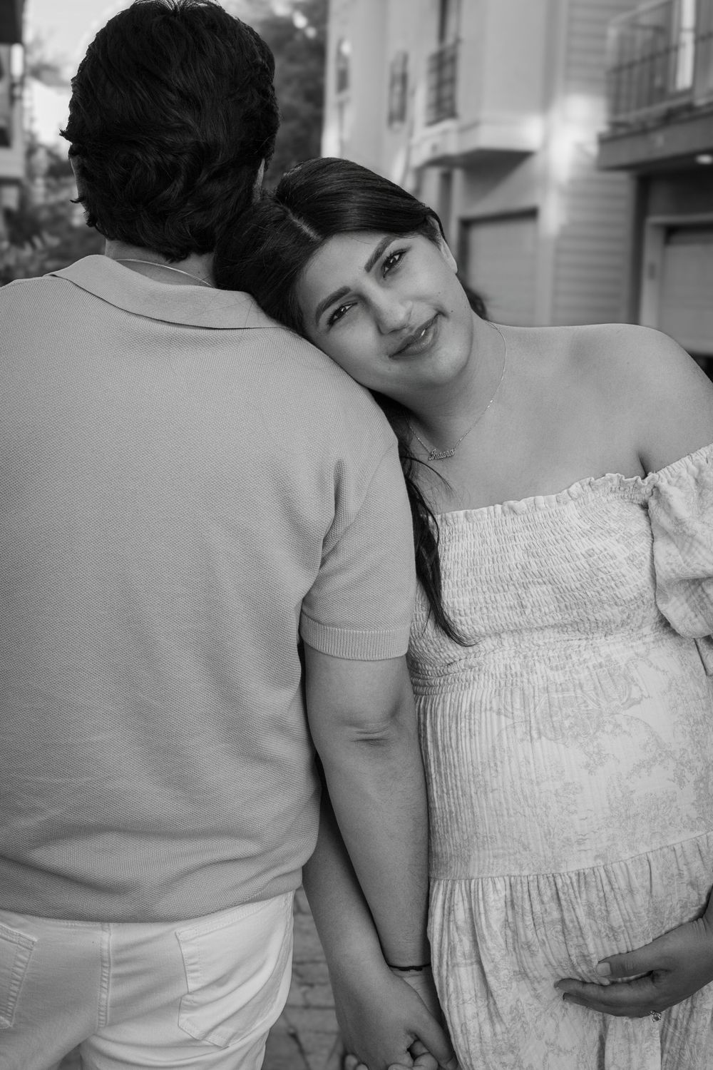 Two people in light colored clothing share an intimate black and white moment outdoors.