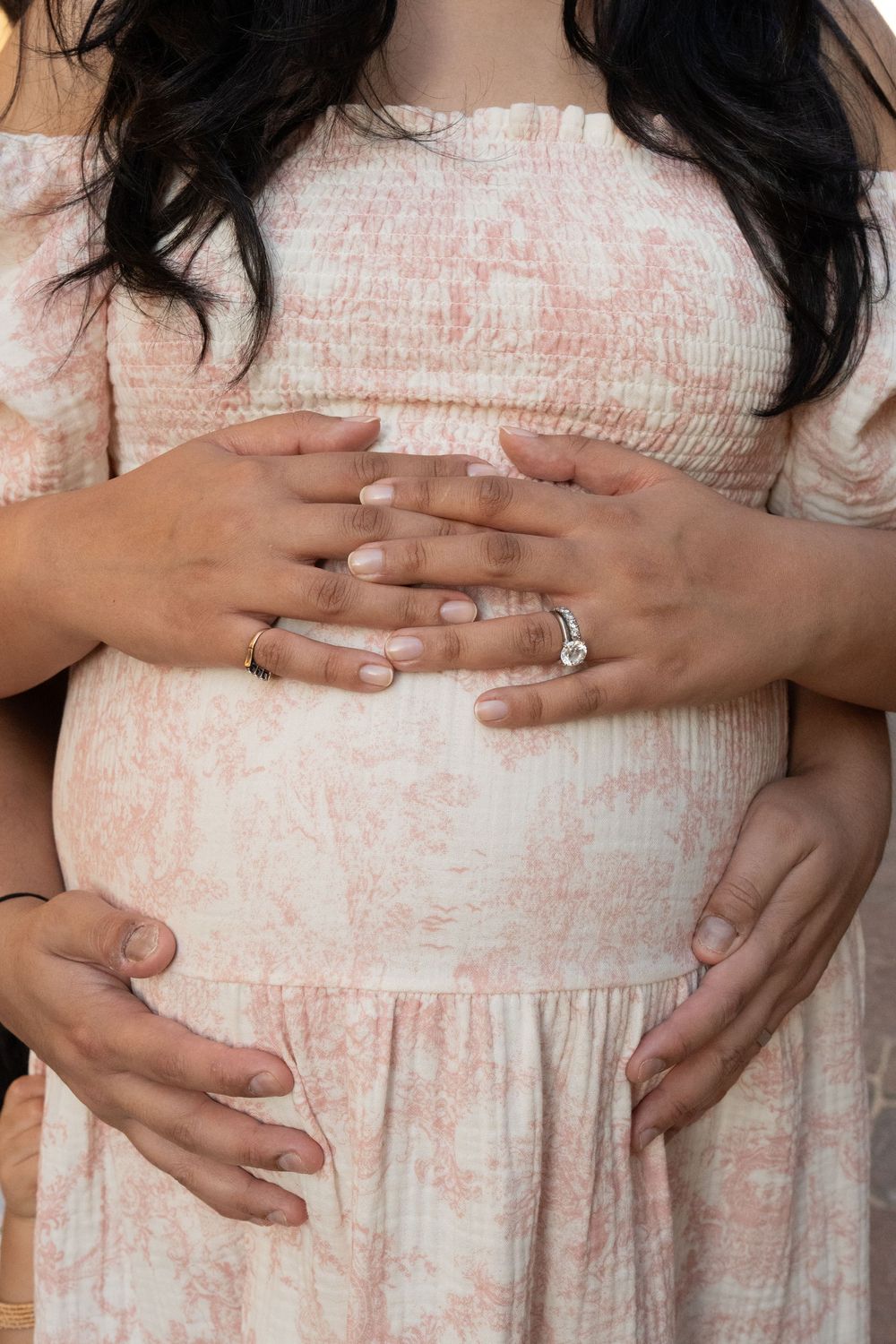 A series of photos showing hands cradling a pregnant belly in a pink and white floral dress.