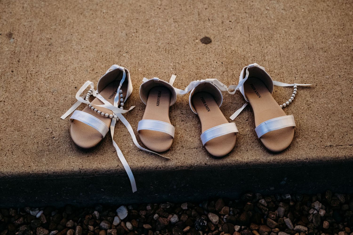 2 pairs of little girls shoes with pearls and ribbon lined up on the patio