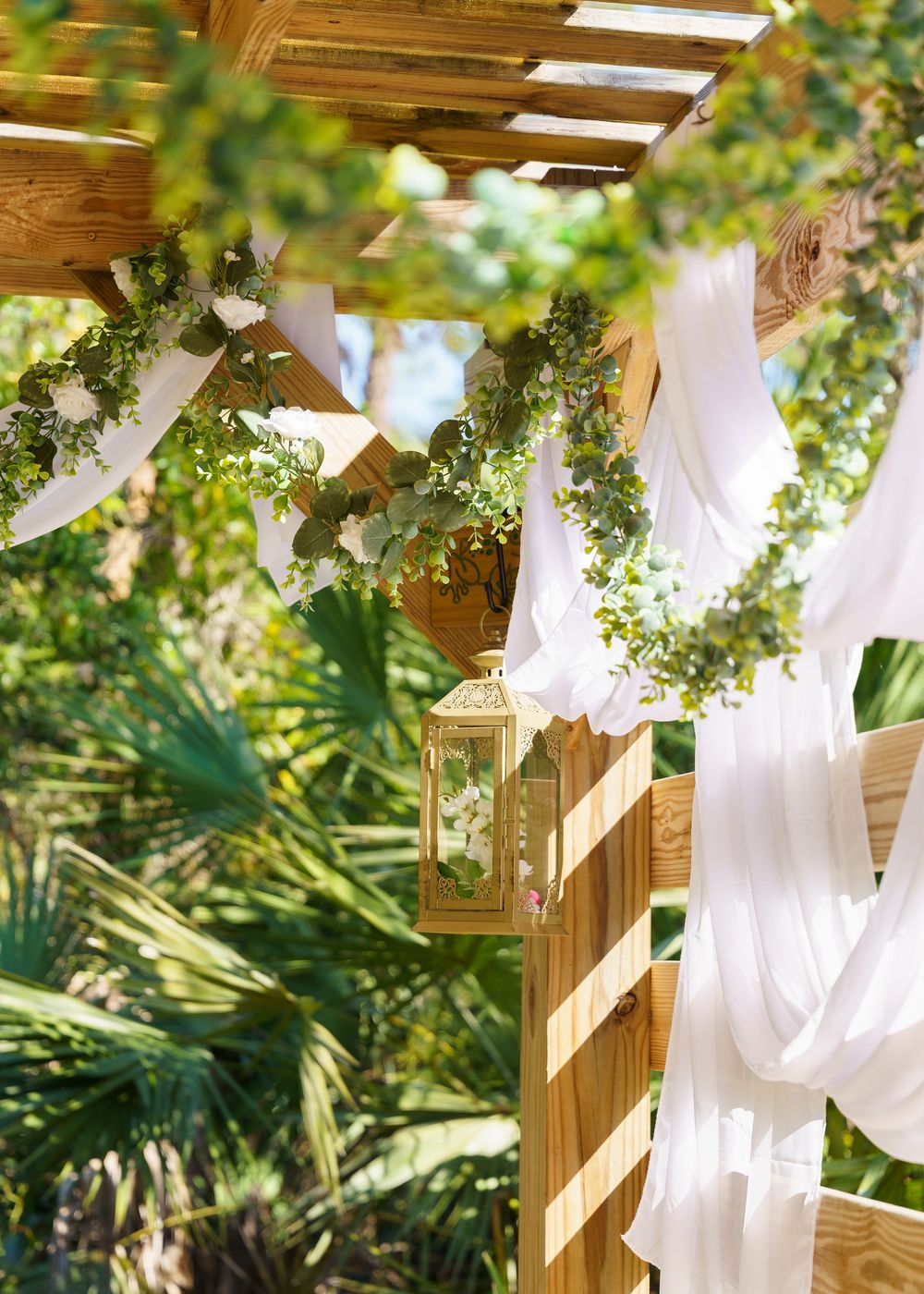 Elegant outdoor wedding ceremony setup with flowing white fabric draping and greenery decorations.