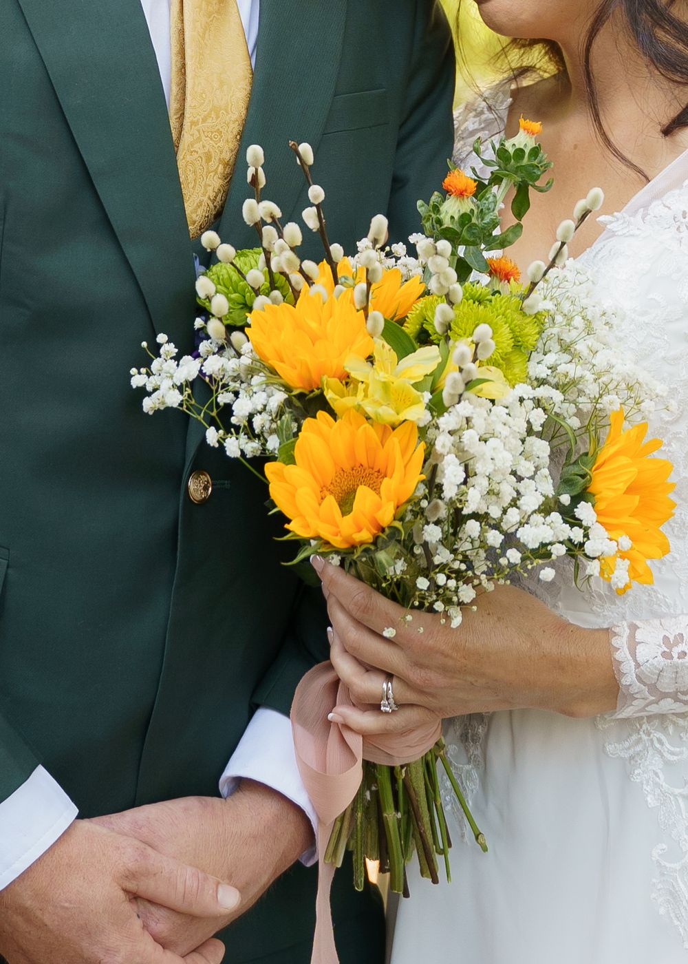 A wedding bouquet featuring bright yellow sunflowers and delicate white baby's breath flowers against formal attire.