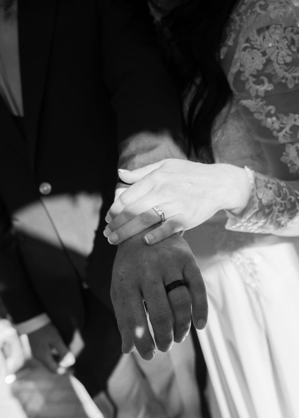 Black and white close-up of hands showing wedding rings during ceremony.