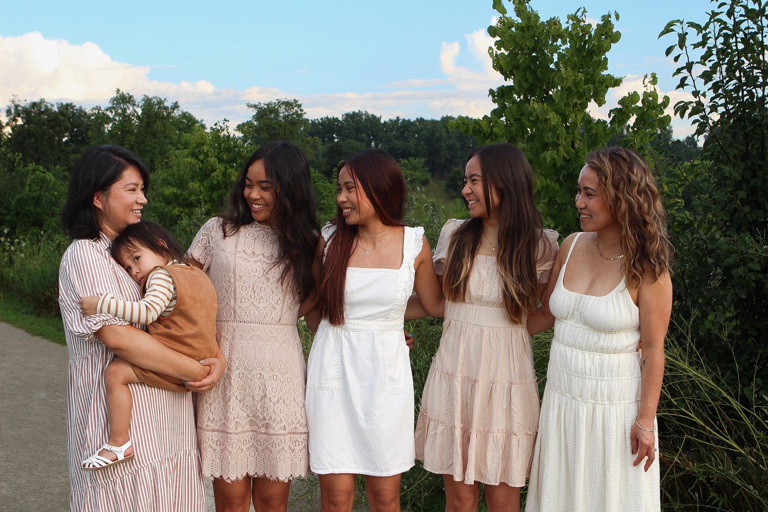 Group photo session in a garden setting with people wearing light colored dresses against green foliage.