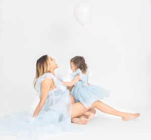 A parent and child in light blue dresses lay together on a white floor during a photo session.
