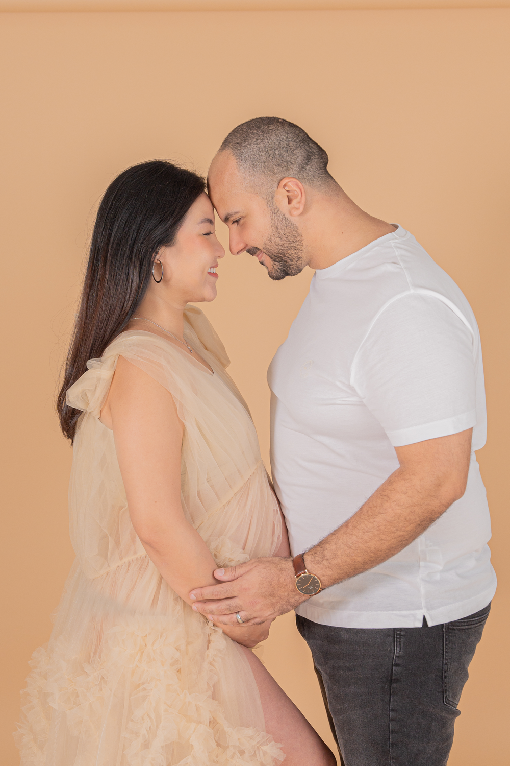 Intimate couple's maternity portraits in neutral tones against peach background.