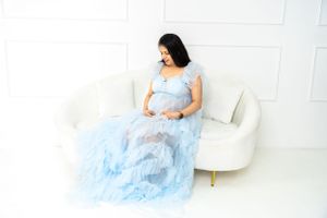 Serene maternity portrait with woman in light blue dress resting on white couch.