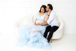 Couple in formal attire cuddle on white couch with flowing blue dress.