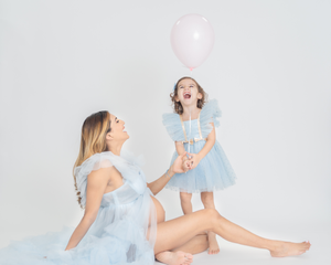Playful mother-child poses in light blue dresses on white background.